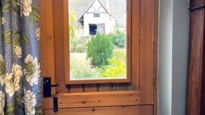 A wooden door with a window, a floral curtain, and a view of a house and greenery. - Luxury Cottage with Pool (Bredon)