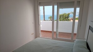 Un dormitorio con cama, puerta corrediza de vidrio que da a un balcón con vista al mar.