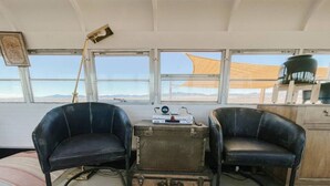 Une pièce avec deux fauteuils en cuir noir, une valise ancienne, une lampe et une fenêtre donnant sur le désert.
