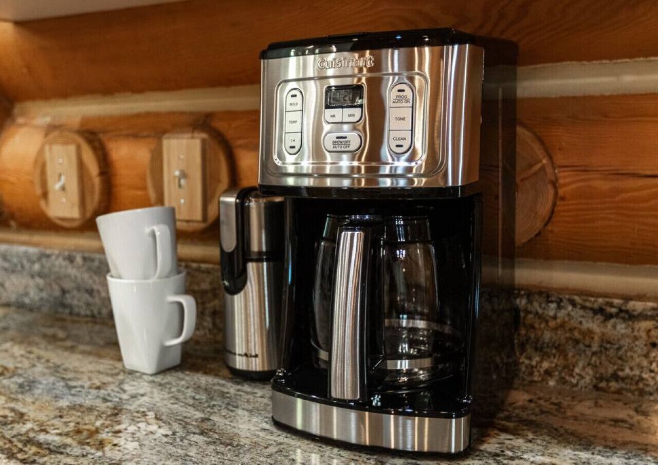 A stainless steel coffee maker with a digital display and control buttons on a granite countertop.