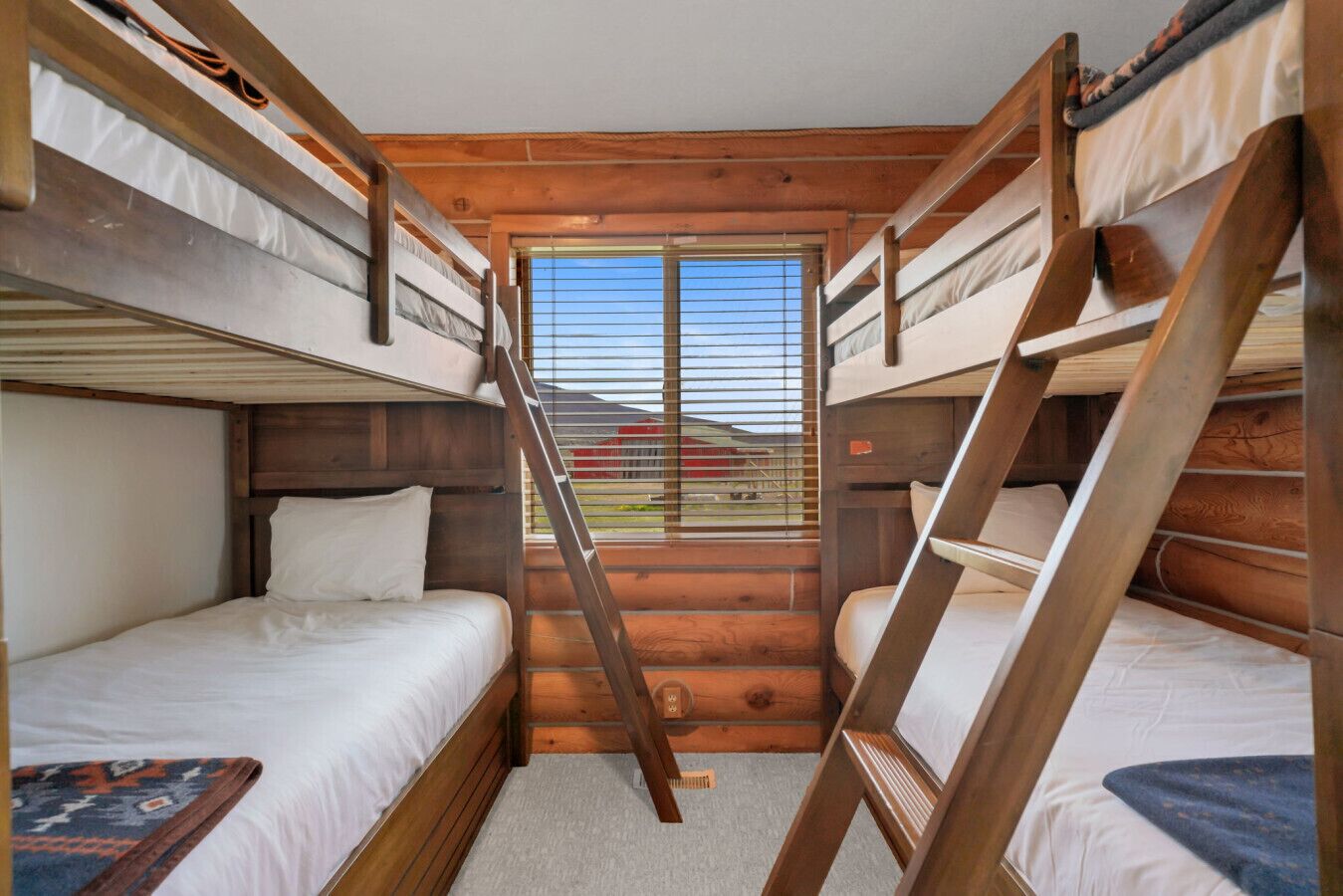 A cabin with bunk beds, a ladder, and a window with a view of a red building.