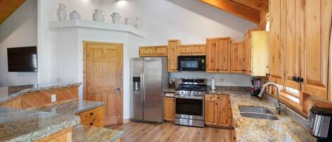 A kitchen with wooden cabinets, granite countertops, a stainless steel refrigerator, a microwave, and an oven.