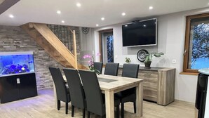 Een moderne keuken met een houten tafel en stoelen, een televisie boven de werkblad bevestigd, en een trap die naar een ander niveau leidt.