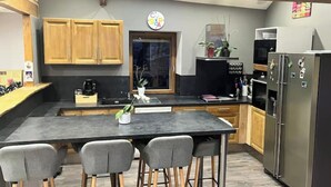 Een moderne keuken met houten kastjes, een centraal eiland met barstoelen, een koelkast en een magnetron.
