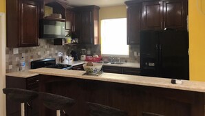 A kitchen with dark wooden cabinets, a black refrigerator, a stove, and a sink. There are bar stools and a window providing natural light. - PALMVILLO MASTER SUIT (dominica)