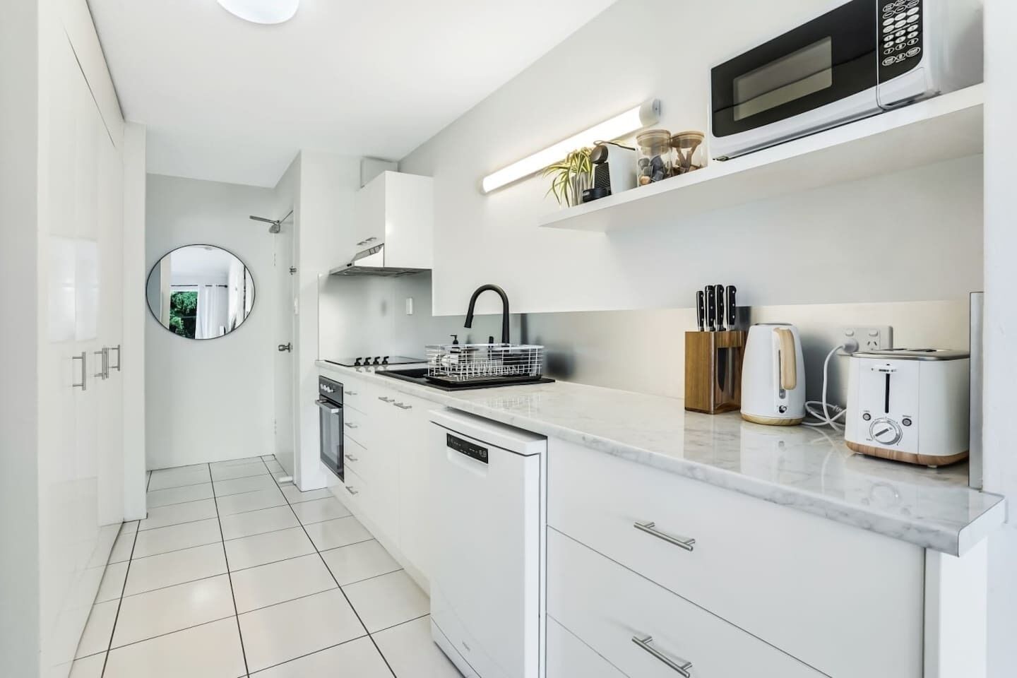 A modern kitchen with white cabinetry, a built-in oven, a microwave, and a toaster.
