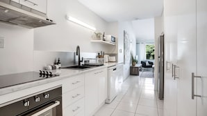 A modern kitchen with white cabinetry, a stainless steel range hood, and a built-in dishwasher.