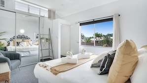 A modern hotel room with a large bed, a balcony with a view, and a separate seating area with a chair and a small table.