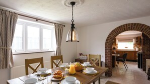 A dining area with a wooden table set for breakfast, a brick archway leading to a kitchen, and a window with curtains. - 3 bedroom accommodation in Llanerfyl, near Welshpool (Llanerfyl, near Welshpool)