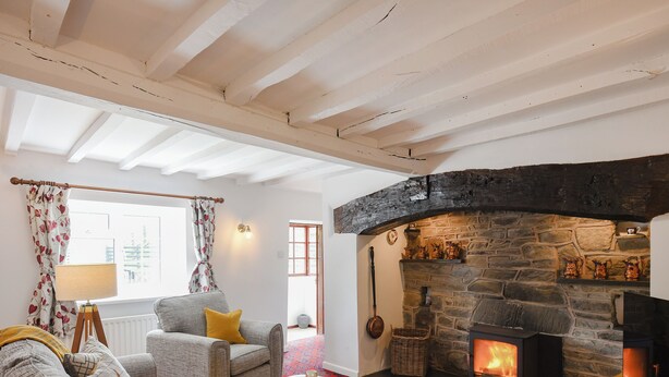 A cozy living room with a stone fireplace, a sofa set, a small table with tea cups, and a window with floral curtains. - 3 bedroom accommodation in Llanerfyl, near Welshpool (Llanerfyl, near Welshpool)