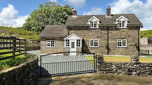 A stone house with a gated entrance, a stone wall, and a grassy hill in the background. - 3 bedroom accommodation in Llanerfyl, near Welshpool (Llanerfyl, near Welshpool)