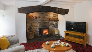 A cozy living room with a stone fireplace, a television, and a dining area with tea set. - 3 bedroom accommodation in Llanerfyl, near Welshpool (Llanerfyl, near Welshpool)