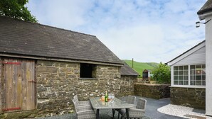 A stone building with a wooden door and a window. There is a table with chairs and a bottle of wine. - 3 bedroom accommodation in Llanerfyl, near Welshpool (Llanerfyl, near Welshpool)