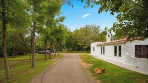 Un camino que lleva a un edificio blanco con tejado de tejas rojas, rodeado de árboles y césped.
