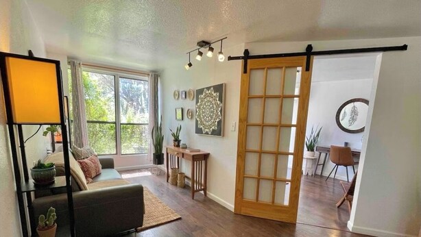 Un salón amplio con un ventanal corredero que da a un comedor, un sofá, una mesa de centro y una estantería.