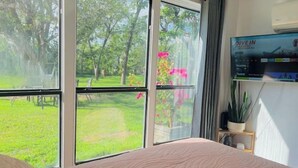 Un dormitorio con un ventanal grande, una cama, un televisor y una planta en maceta.