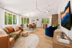 A spacious living area with a sofa, dining table, chairs, and a TV.