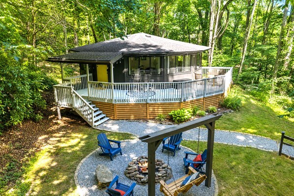 A cabin with a deck, outdoor seating, and a fire pit.