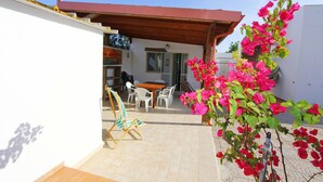 A patio area with a table and chairs, a wooden pergola, and a potted bougainvillea plant. - Myrtle House1318 (Torre Pali)