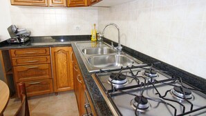 A kitchen with wooden cabinets, a stainless steel sink, and a gas stove. - Myrtle House1318 (Torre Pali)