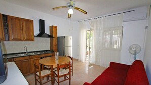 A compact kitchen with wooden cabinets, a refrigerator, a dining table with chairs, a ceiling fan, and a red sofa. - Myrtle House1318 (Torre Pali)