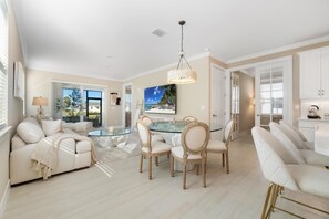 Un salon spacieux avec une table basse à plateau en verre, un canapé beige et un coin repas comprenant une table et des chaises, le tout avec des plateaux en verre.