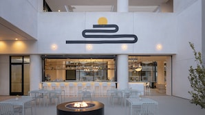 An outdoor seating area with a fire pit, white chairs, and a bar with a modern design. - Drift Palm Springs, a Member of Design Hotels (Palm Springs)