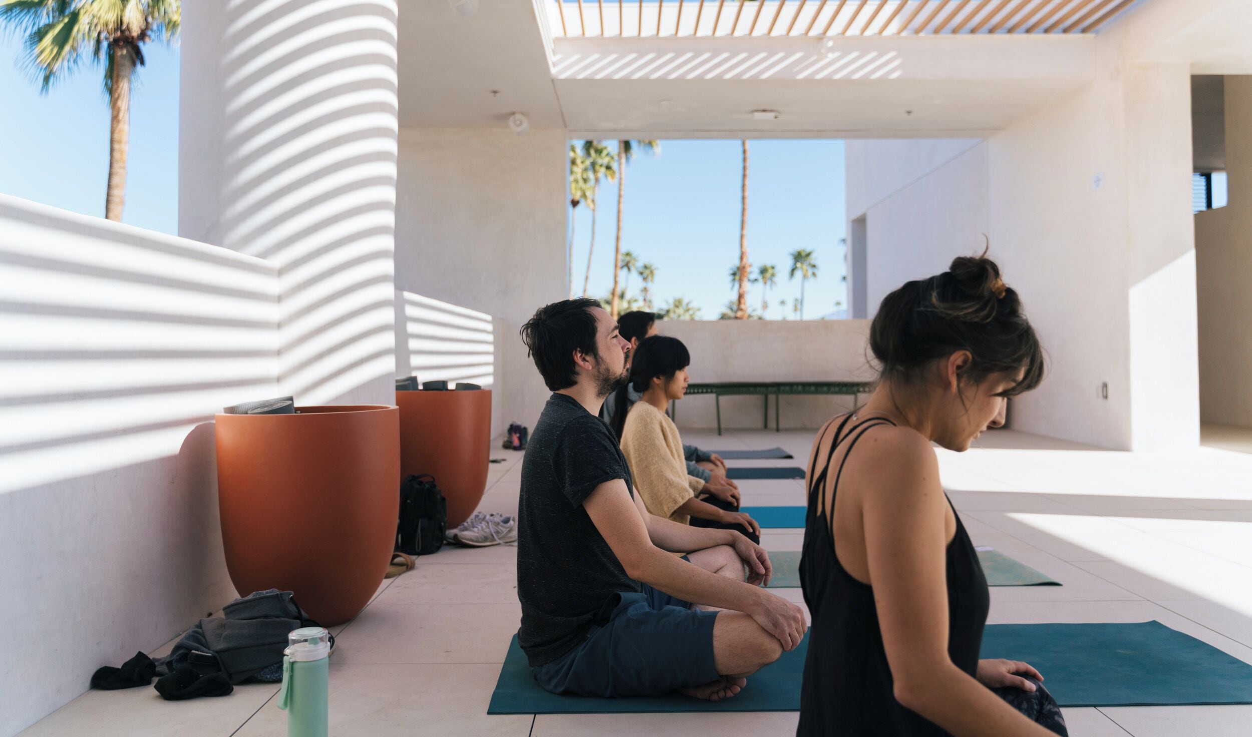 A modern indoor yoga space with a minimalist design, featuring large windows and a view of palm trees.