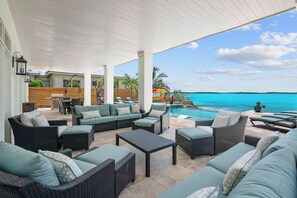 An outdoor patio with wicker furniture, a pool, and a view of the ocean. - Newly Built Luxury 5- bedroom Beachfront Villa with Infinity Heated Pool (Exuma)