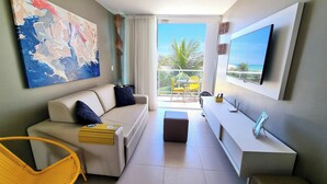 A modern living room with a sofa, a yellow chair, a flat-screen TV, and a balcony with a view of the ocean. - Lindo Apartamento com Varanda e Vista Mar (Barra de São Miguel)