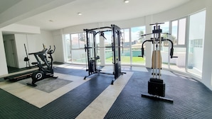 A gym with cardio machines, weightlifting equipment, and large windows offering a view of the outdoors. - Lindo Apartamento com Varanda e Vista Mar (Barra de São Miguel)