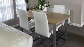 Een moderne eetruimte met een houten tafel, witte stoelen, een hangende lamp en een bloempot.