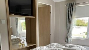 Een slaapkamer met een bed, een tv aan de muur, een raam met gordijnen en een nachtkastje met een lamp.