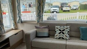 A cozy living area with a sofa, a coffee table, and a window with curtains. - M697 - 8 berth with veranda - Pet Friendly (Camber)
