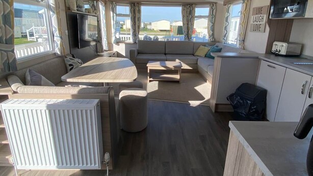 A spacious RV interior with a living area, kitchenette, and large windows offering views of the outside. - M697 - 8 berth with veranda - Pet Friendly (Camber)