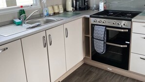 A compact kitchen with wooden cabinets, a stainless steel sink, a coffee maker, a kettle, and a built-in oven. - M697 - 8 berth with veranda - Pet Friendly (Camber)