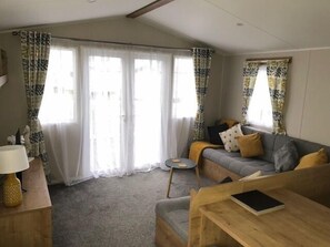 A living room with a sofa, a small table, and a lamp. There are curtains on the windows.