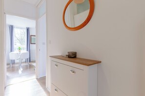 Une pièce comprenant une coiffeuse en bois, un miroir et donnant sur un coin repas avec une table et des chaises.