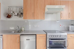 Une cuisine moderne avec des meubles en bois, un lave-vaisselle en acier inoxydable, un four et une hotte aspirante.
