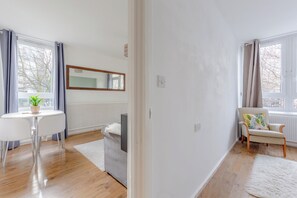 Un salon moderne avec un canapé blanc, une table à manger avec des chaises, une plante en pot et une grande fenêtre avec des rideaux.