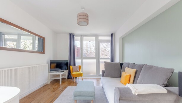 Un salon moderne avec un canapé gris, un fauteuil jaune, une table basse blanche et un téléviseur posé sur un meuble blanc.