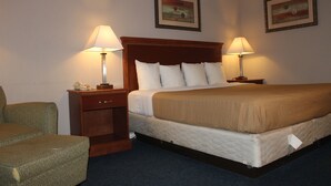 Habitación de hotel con una cama grande, dos mesitas de noche con lámparas, una silla y dos cuadros en la pared.