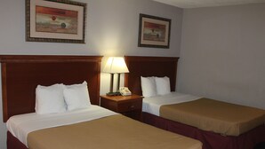 Habitación de hotel con dos camas individuales, cada una con cabecero de madera, ropa de cama blanca y manta marrón. Entre las camas, una mesita de noche con lámpara y teléfono.