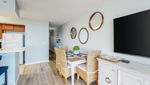 A modern kitchen with white cabinets, a dining area with wicker chairs, and a large flat-screen TV mounted on the wall. - Destin West - Sandpiper 407 (Okaloosa Island)