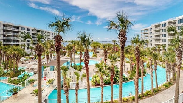 A resort with multiple swimming pools surrounded by palm trees and modern buildings. - Destin West - Sandpiper 407 (Okaloosa Island)