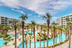 A resort with multiple swimming pools surrounded by palm trees and modern buildings. - Destin West - Sandpiper 407 (Okaloosa Island)
