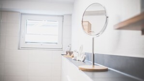 A bathroom with a window, a round mirror, and a countertop with toiletries. - Modern vacation apartment Knüllwald (Knüllwald)