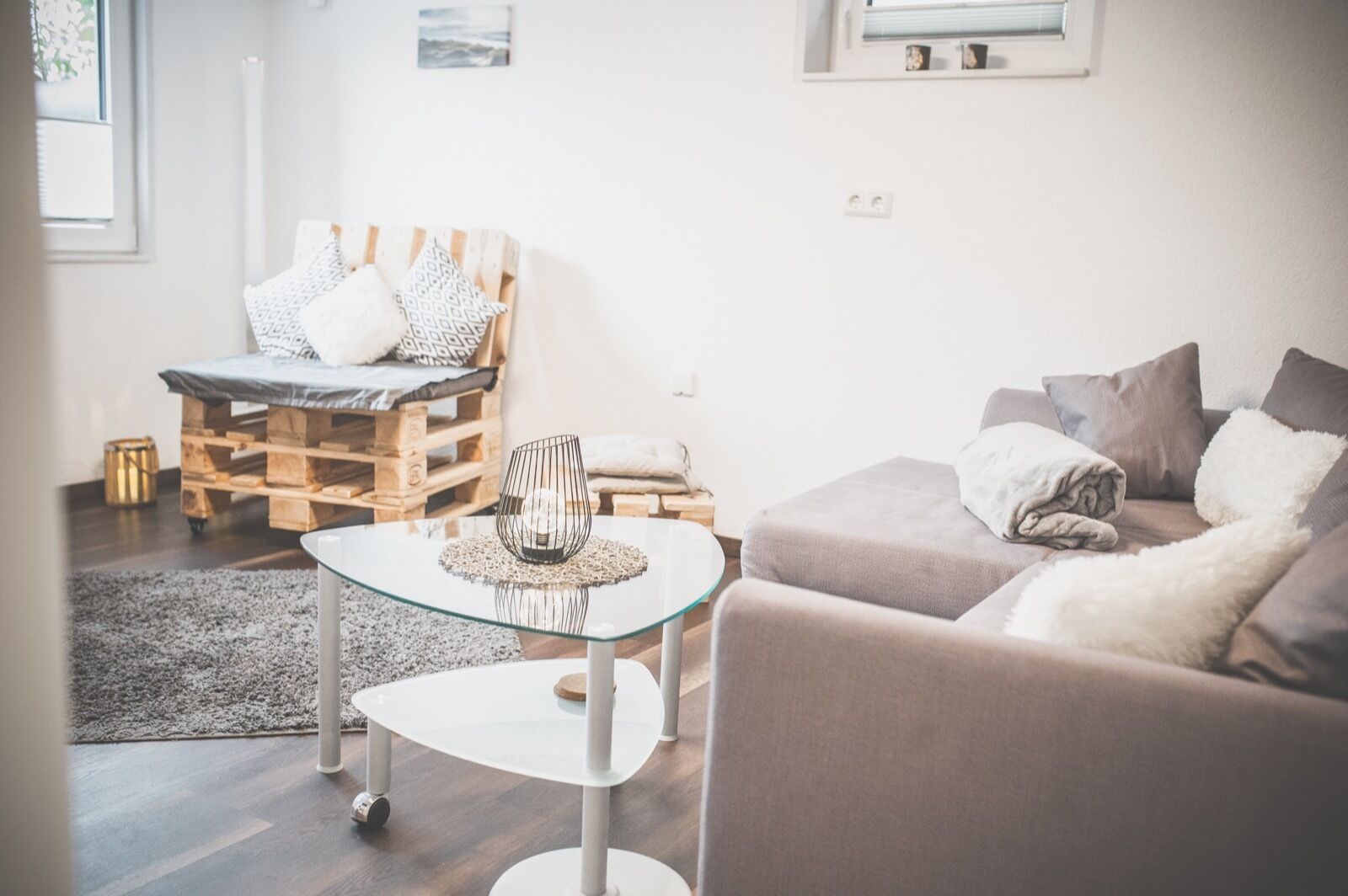 Ein modernes Wohnzimmer mit einem Glastisch, einer Couch und einem Bett aus Holzpaletten.