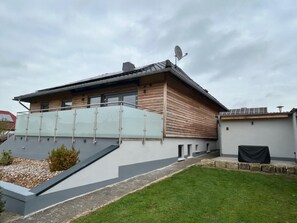 Une maison moderne avec un toit en pente, un balcon doté de rampes en verre et une antenne parabolique.