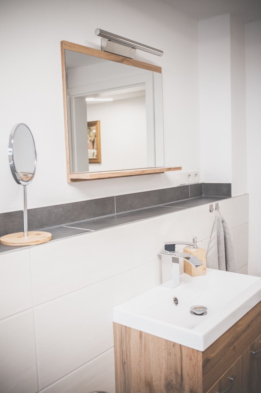 A modern bathroom with a wooden vanity, a mirror, and a towel rack.